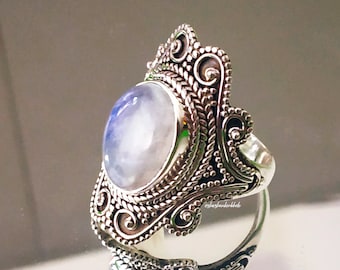 May include: A silver ring with an ornate design and a large, oval-shaped moonstone.