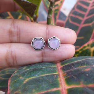 Op de afbeelding: Een paar zilveren oorbel studs met zeshoekige instellingen en ronde, lichtpaarse edelstenen.
