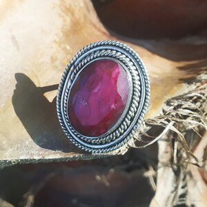 May include: A silver ring with a large, oval-shaped, dark pink gemstone set in a twisted silver band.