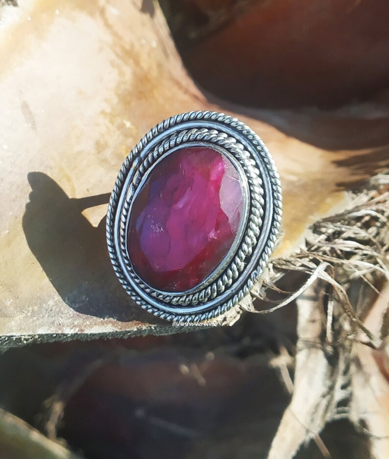 May include: A silver ring with a large, oval-shaped, dark pink gemstone set in a twisted silver band.