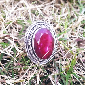 Op de afbeelding: Een zilveren ring met een grote, ovale, dieprode edelsteen gezet in een decoratieve zilveren zetting.