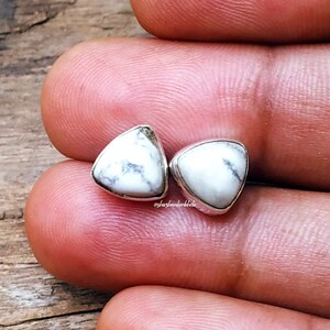 Op de afbeelding: Een paar zilveren driehoekige oorbel studs met witte howliet stenen. De stenen hebben een natuurlijk marmerpatroon.