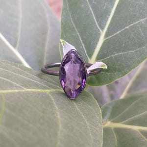 Op de afbeelding: Een zilveren ring met een marquise-vormige amethist edelsteen. De ring ligt op een groen blad.