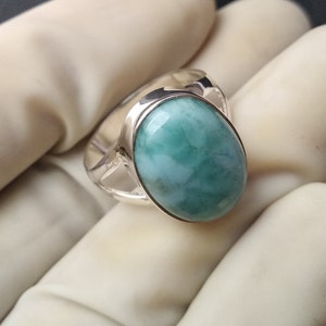 May include: A silver ring with a light blue and green oval gemstone. The ring has a simple design with a smooth band.