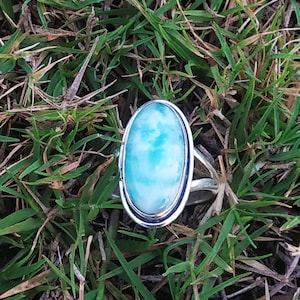 May include: A silver ring with a large oval-shaped blue and green gemstone. The ring is set in a silver band with a smooth finish.