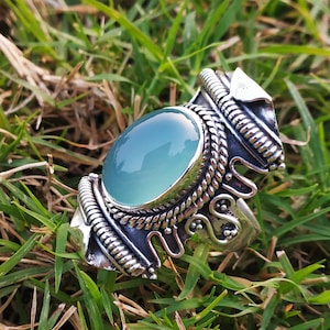 May include: A silver ring with a large, oval-shaped, light blue gemstone set in a decorative, ornate silver band.