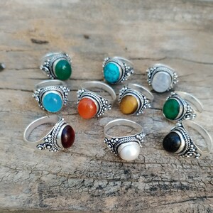 Puede incluir: Diez anillos de plata con piedras preciosas de diferentes colores. Los anillos tienen una banda de plata decorativa con un diseño en relieve. Las piedras preciosas son turquesa, verde, naranja, roja, blanca, azul, negra y marrón.