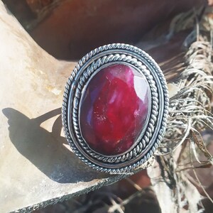 May include: A silver ring with a large, oval-shaped, red gemstone set in a twisted silver band.
