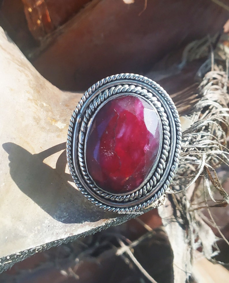 May include: A silver ring with a large, oval-shaped, red gemstone set in a twisted silver band.