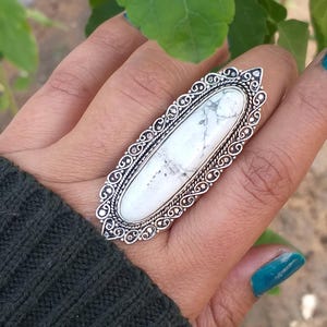 Pode incluir: Um anel de prata com uma pedra oval de howlite branca engastada em um design filigranado detalhado.