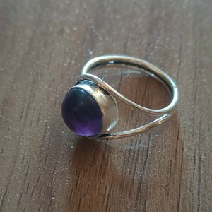 Op de afbeelding: Een zilveren ring met een paarse amethist edelsteen. De ring heeft een eenvoudig, delicaat ontwerp.