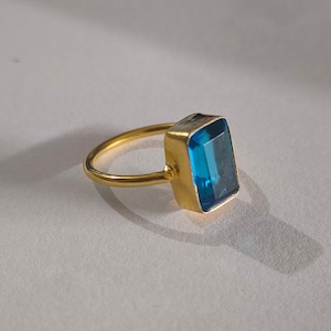 May include: A gold ring with a large, rectangular, blue gemstone.