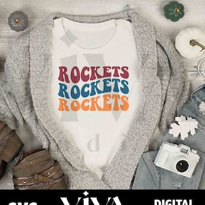 May include: A white t-shirt with the words "ROCKETS" repeated three times in a retro font. The words are stacked on top of each other and are in different colors: maroon, blue, and orange.