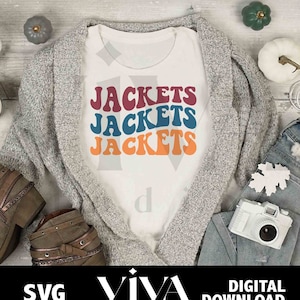 May include: A white t-shirt with the text "Jackets" repeated three times in a retro font. The text is in red, blue, and orange. The t-shirt is on a gray cardigan with a pair of brown boots and a camera on a blue denim background.