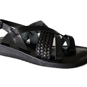 May include: Black leather sandals with a braided strap design and an adjustable ankle strap. The sandals have a flat sole.