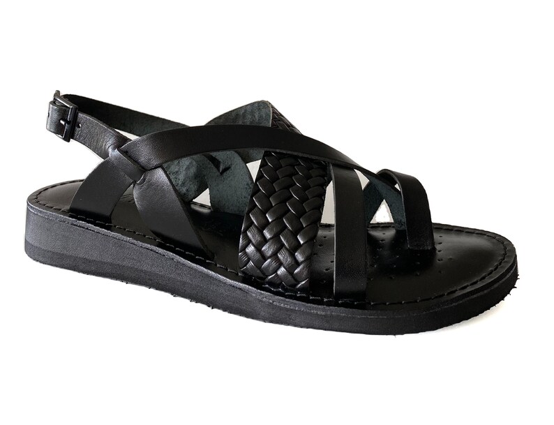 May include: Black leather sandals with a braided strap design and an adjustable ankle strap. The sandals have a flat sole.
