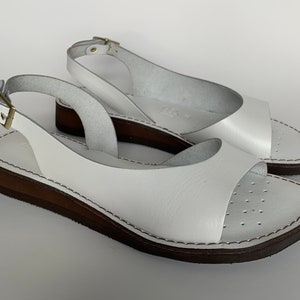 Puede incluir: Sandalias blancas de cuero con una correa de slingback y una suela de plataforma marr&oacute;n.