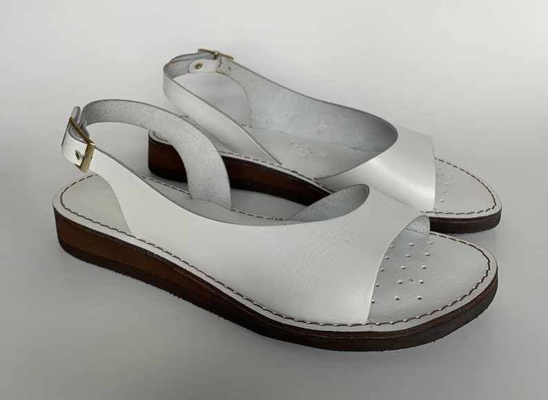 Puede incluir: Sandalias blancas de cuero con una correa de slingback y una suela de plataforma marr&oacute;n.
