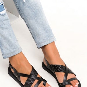 May include: Black leather sandals with a woven strap design. The sandals have a toe loop and an ankle strap.