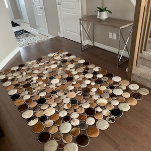 May include: A large, brown and white cowhide rug made of many round pieces of hide. The rug is laid out on a hardwood floor in a hallway.