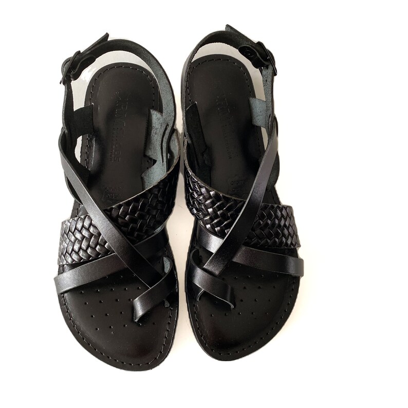 May include: A pair of black leather sandals with criss-cross straps and a woven design.