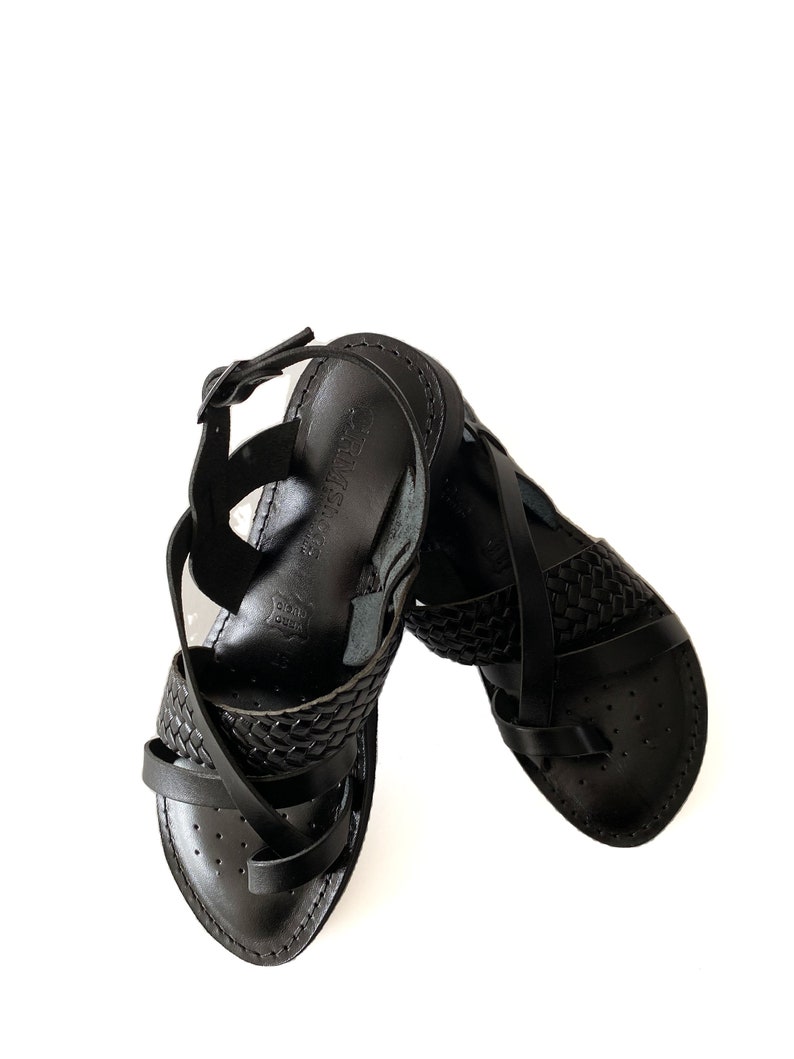 May include: Black leather sandals with a woven strap design. The sandals have a buckle closure and a pointed toe.