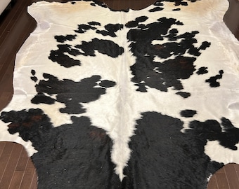 Puede incluir: Alfombra de piel de vaca negra y blanca con una textura natural y peluda. La alfombra tiene un patrón único de parches negros y blancos.