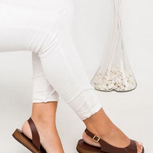 Puede incluir: Sandalias de cuero marr&oacute;n con una correa de hebilla y un dedo del pie abierto. Las sandalias tienen una suela plana y una correa de slingback.