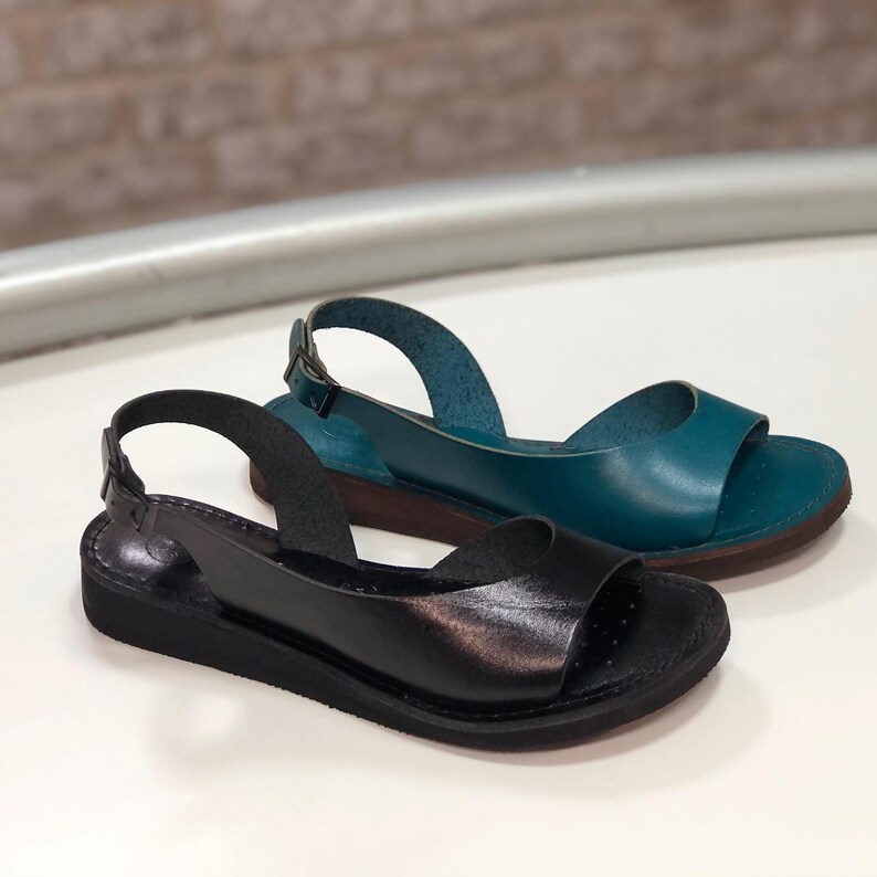 Puede incluir: Dos pares de sandalias de cuero con una correa de slingback. Un par es negro y el otro es azul verdoso.