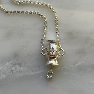 Puede incluir: Un collar de plata con un colgante de urna detallado y una piedra de aguamarina en forma de l&aacute;grima colgante.