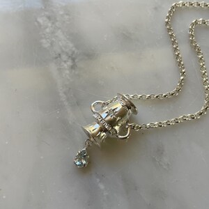 Puede incluir: Un collar de plata con un colgante de urna detallado y una piedra preciosa azul claro en forma de l&aacute;grima.