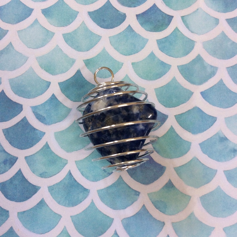 May include: A blue and white gemstone is encased in a silver wire cage. The cage is suspended from a silver loop. The gemstone is in the shape of a teardrop.