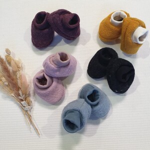 Könnte beinhalten: Sechs Paar Babyschuhe in verschiedenen Farben, darunter Lila, Rosa, Blau, Schwarz und Gelb. Die Schuhe sind aus weichem, flauschigem Stoff und haben einen umgeschlagenen Bund.