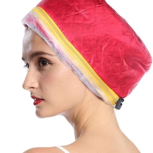 May include: A red quilted hair treatment cap with a yellow zipper and clear plastic lining. The cap is designed to cover the head and is worn by a person in the image.