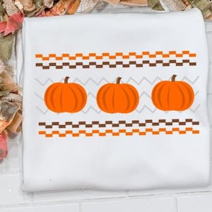 May include: White t-shirt with a brown and orange geometric pattern and three orange pumpkins.