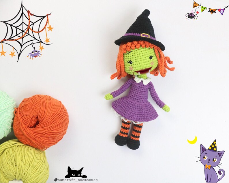 Puede incluir: Una mu&ntilde;eca de bruja de crochet con piel verde, cabello naranja, un vestido morado y medias a rayas negras y naranjas. La mu&ntilde;eca lleva un sombrero de bruja negro con una banda marr&oacute;n. La mu&ntilde;eca est&aacute; de pie sobre un fondo blanco.