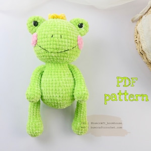 Puede incluir: Un juguete de amigurumi de rana de crochet verde con una corona amarilla, mejillas rosadas y ojos negros. El juguete está sentado sobre una superficie blanca. El texto "PDF pattern" está escrito en letras amarillas sobre la superficie blanca. El texto "INS @bumcraft_boomhouse Web bumcraftcrochet.com" está escrito en letras negras sobre la superficie blanca.