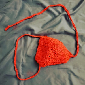 May include: A red crocheted triangle-shaped hat with long ties.