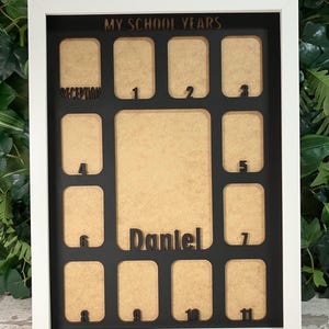 May include: A white rectangular picture frame featuring a black insert with the text MY SCHOOL YEARS at the top. The frame contains multiple cutouts for photos labeled Reception through 11, with a central cutout featuring the name Daniel.
