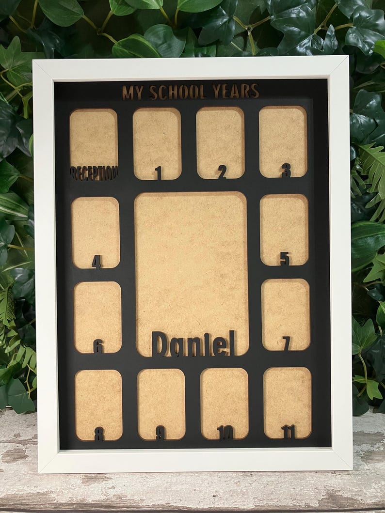 May include: A white rectangular picture frame featuring a black insert with the text MY SCHOOL YEARS at the top. The frame contains multiple cutouts for photos labeled Reception through 11, with a central cutout featuring the name Daniel.