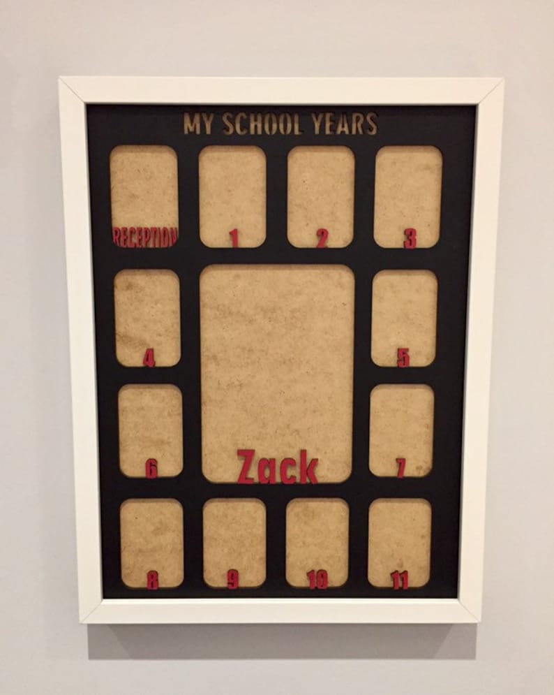 May include: A white rectangular frame containing a black mat with the text MY SCHOOL YEARS at the top. The mat features twelve small rectangular openings labeled with red numbers from 1 to 11 and the word RECEPTION, plus a large central opening with the name Zack in red.