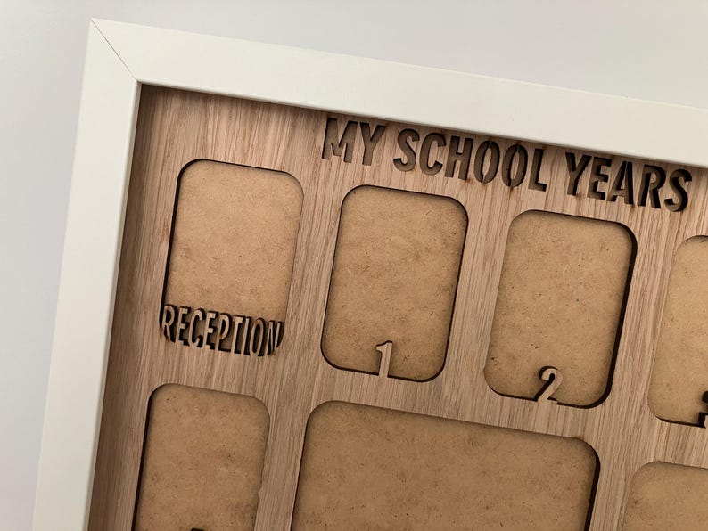May include: A white-framed wooden display board with the laser-cut text MY SCHOOL YEARS at the top. The board features multiple rectangular cutouts for photographs, with the labels RECEPTION, 1, and 2 engraved below specific openings.