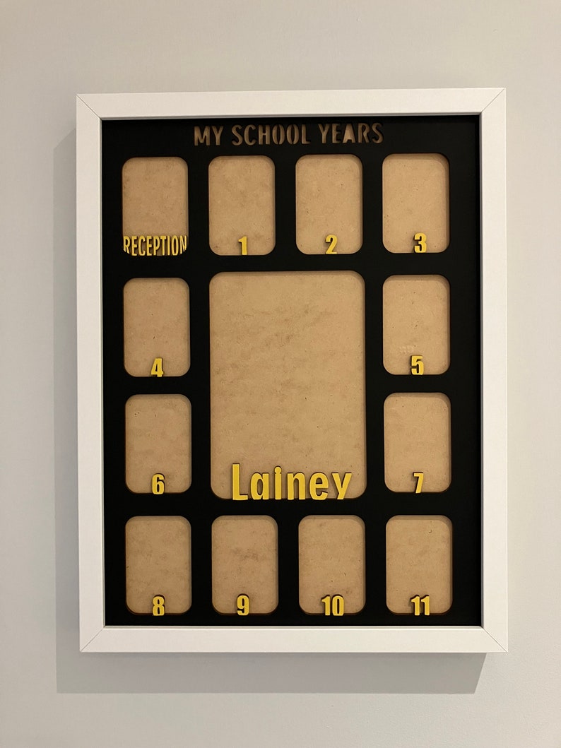 May include: A white rectangular picture frame with a black mat featuring the text MY SCHOOL YEARS at the top. It includes twelve small photo slots labeled Reception through 11 in gold, plus a larger central slot with the name Lainey in gold.