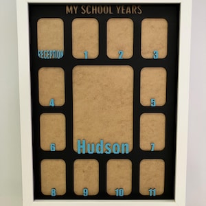 May include: A white rectangular picture frame with a black mat featuring the text MY SCHOOL YEARS at the top and the name Hudson in the center. It contains twelve small photo slots labeled Reception through 11 in light blue lettering.