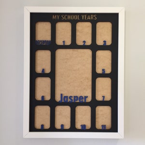 May include: A white rectangular picture frame with a black mat board featuring the text MY SCHOOL YEARS at the top. The mat has twelve small photo openings labeled with blue numbers from 1 to 11 and the word RECEPTION, plus a large central opening with the name Jasper in blue.