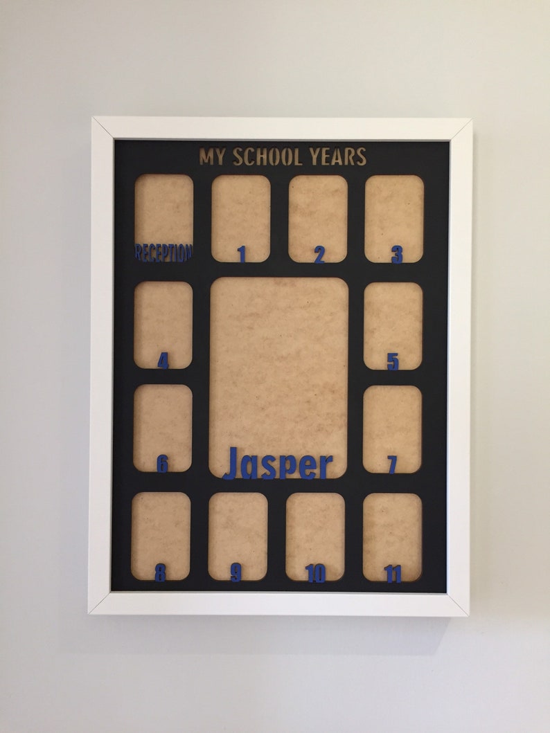 May include: A white rectangular picture frame with a black mat board featuring the text MY SCHOOL YEARS at the top. The mat has twelve small photo openings labeled with blue numbers from 1 to 11 and the word RECEPTION, plus a large central opening with the name Jasper in blue.