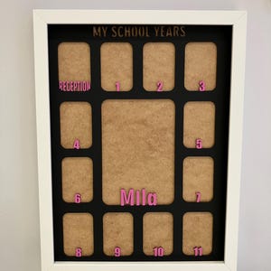 May include: A white framed collage picture board titled MY SCHOOL YEARS in gold lettering. It features a black background with twelve small rectangular photo slots and one large central slot. Pink labels mark Reception through year 11, with the name Mila in pink.