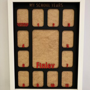 May include: A white rectangular frame containing a black mat with the text MY SCHOOL YEARS at the top. It features twelve small photo slots labeled Reception through 11 in red, plus a large central slot with the red name Finley printed below.