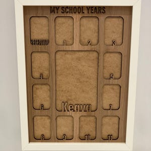 May include: A white-framed wooden display board titled MY SCHOOL YEARS with cutouts for photos. It features a large central space, a name cutout for Keava, and smaller labeled slots for Reception through year 11, organized in a grid layout.