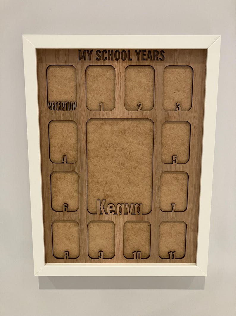 May include: A white-framed wooden display board titled MY SCHOOL YEARS with cutouts for photos. It features a large central space, a name cutout for Keava, and smaller labeled slots for Reception through year 11, organized in a grid layout.